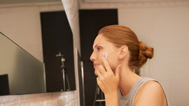 Vrouw smeert crème op haar gezicht voor de spiegel 